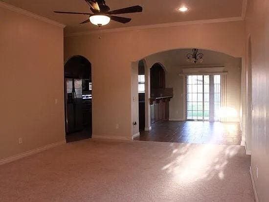 spare room featuring baseboards, arched walkways, ornamental molding, dark carpet, and ceiling fan with notable chandelier