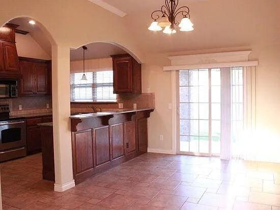 kitchen featuring hanging light fixtures, arched walkways, stainless steel appliances, and decorative backsplash