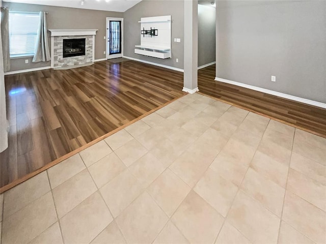 unfurnished living room with vaulted ceiling, a stone fireplace, and light hardwood / wood-style floors