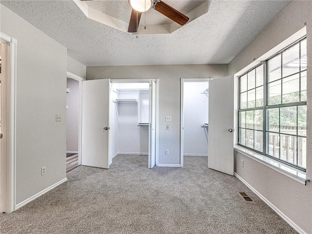 unfurnished bedroom with ceiling fan, a spacious closet, a textured ceiling, and light carpet