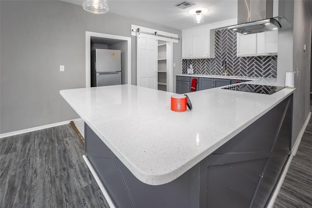 kitchen featuring a barn door, kitchen peninsula, stainless steel refrigerator, white cabinetry, and island range hood