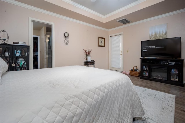 bedroom featuring visible vents, a raised ceiling, wood finished floors, and ornamental molding