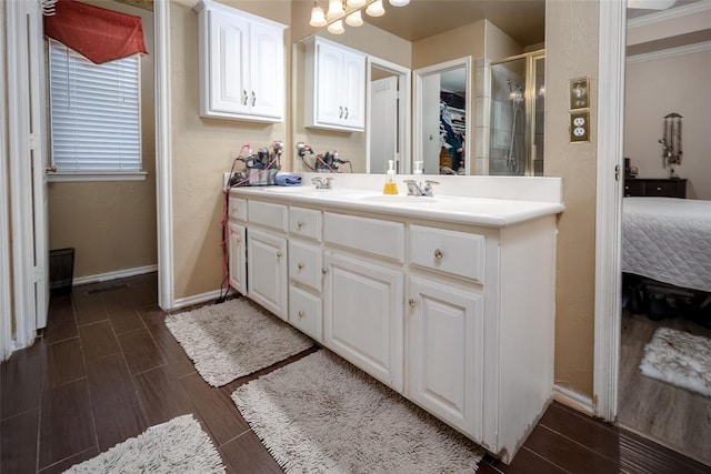 ensuite bathroom featuring wood finish floors, a stall shower, vanity, ensuite bath, and baseboards