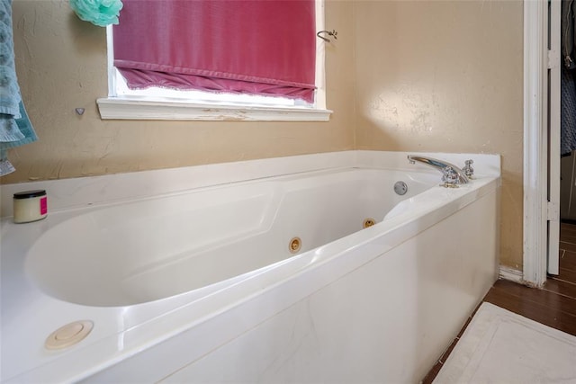 bathroom featuring a healthy amount of sunlight, a tub with jets, and a textured wall