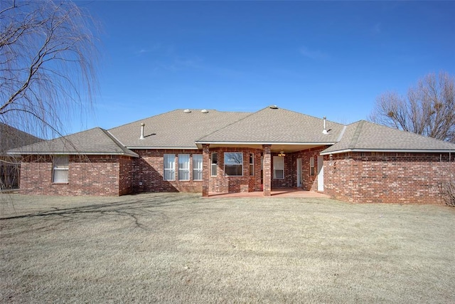 rear view of house with brick siding, a lawn, a patio, and roof with shingles