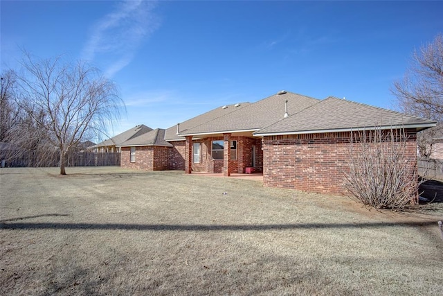 rear view of house with roof with shingles, brick siding, a lawn, and fence