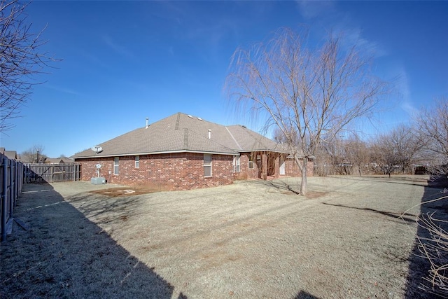 rear view of house featuring brick siding, fence, and driveway