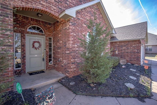 entrance to property with a shingled roof and brick siding