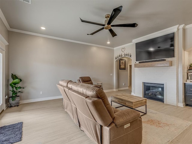 living room featuring ceiling fan, a brick fireplace, ornamental molding, and light hardwood / wood-style floors