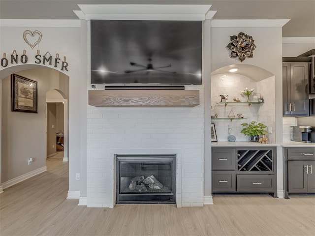 bar with a brick fireplace, gray cabinets, ornamental molding, and light hardwood / wood-style flooring