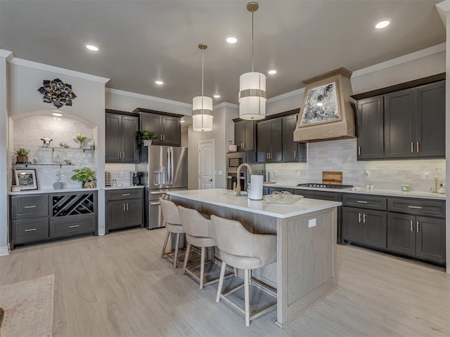 kitchen featuring custom exhaust hood, stainless steel appliances, tasteful backsplash, hanging light fixtures, and a kitchen island with sink