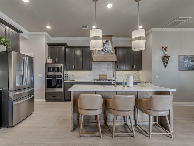 kitchen featuring a center island with sink, appliances with stainless steel finishes, tasteful backsplash, custom range hood, and pendant lighting