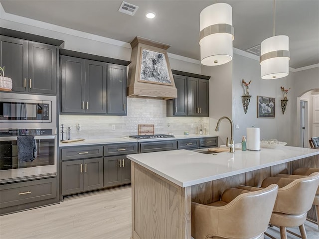 kitchen with decorative backsplash, sink, hanging light fixtures, appliances with stainless steel finishes, and an island with sink