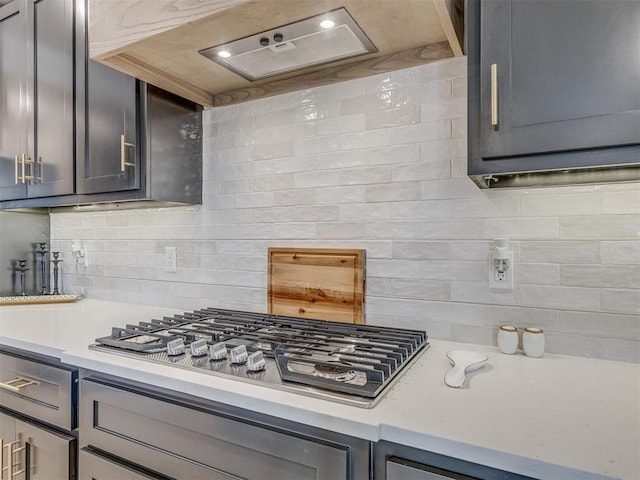 kitchen with decorative backsplash, stainless steel gas stovetop, gray cabinetry, and wall chimney exhaust hood