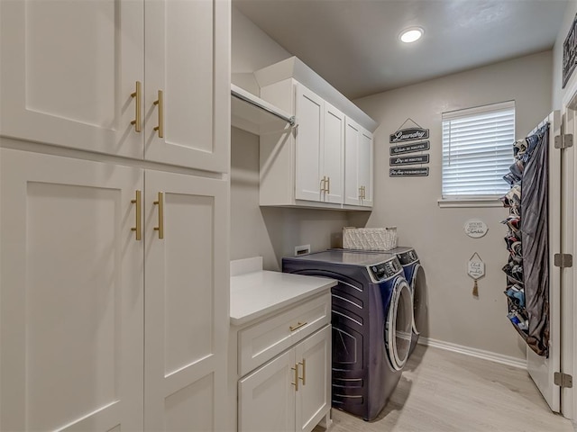 clothes washing area with washing machine and dryer, light hardwood / wood-style floors, and cabinets