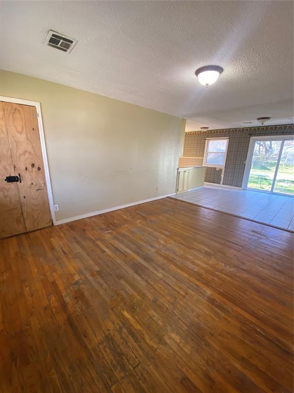 unfurnished living room featuring visible vents, a textured ceiling, baseboards, and wood-type flooring