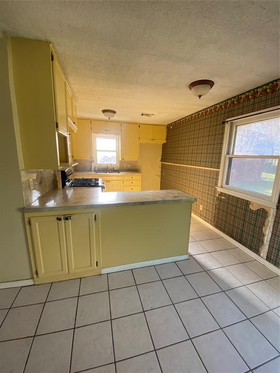 kitchen featuring cream cabinets, gas stove, a peninsula, light tile patterned flooring, and light countertops