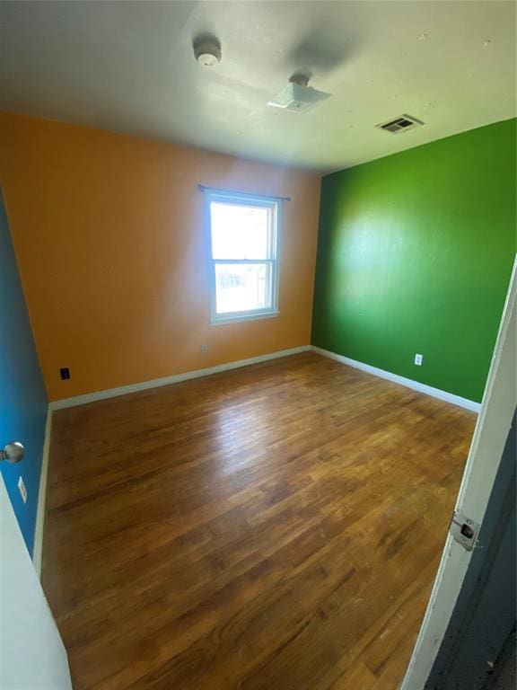 unfurnished room featuring visible vents, baseboards, and wood finished floors