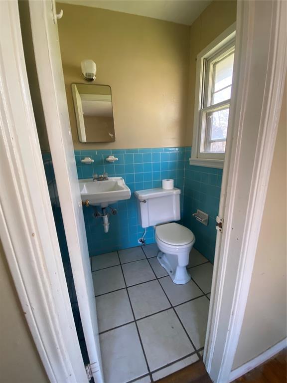 bathroom with tile patterned floors, toilet, a sink, tile walls, and wainscoting