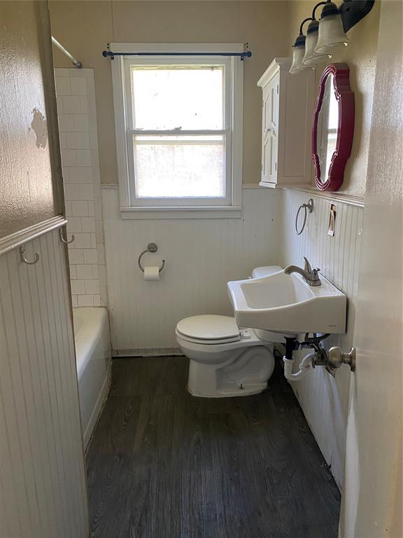 full bathroom featuring a wainscoted wall, toilet, wood finished floors, washtub / shower combination, and a sink