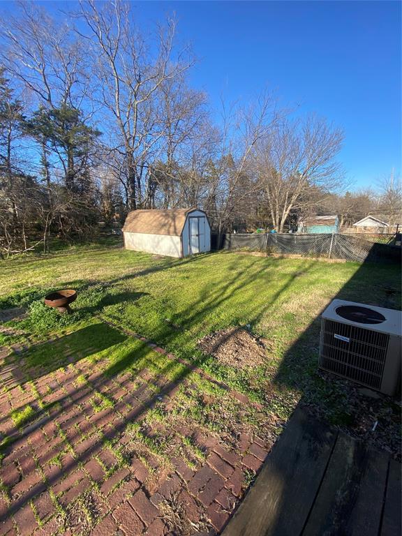 view of yard with a storage unit, an outbuilding, central AC, and fence