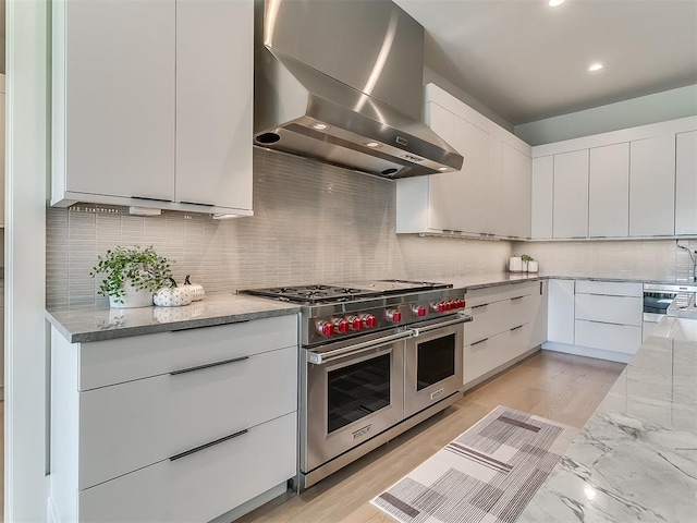 kitchen with light stone counters, double oven range, white cabinetry, and range hood