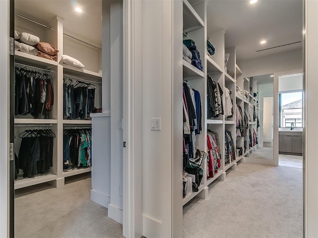 walk in closet with light colored carpet and sink