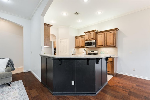 kitchen featuring dark hardwood / wood-style floors, a kitchen breakfast bar, kitchen peninsula, stainless steel appliances, and backsplash