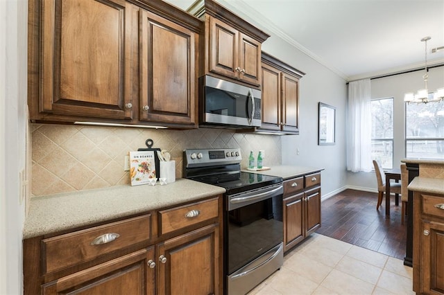 kitchen featuring crown molding, a chandelier, appliances with stainless steel finishes, pendant lighting, and backsplash