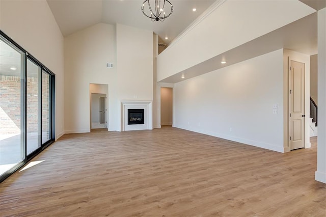 unfurnished living room with light wood-type flooring, high vaulted ceiling, and a notable chandelier