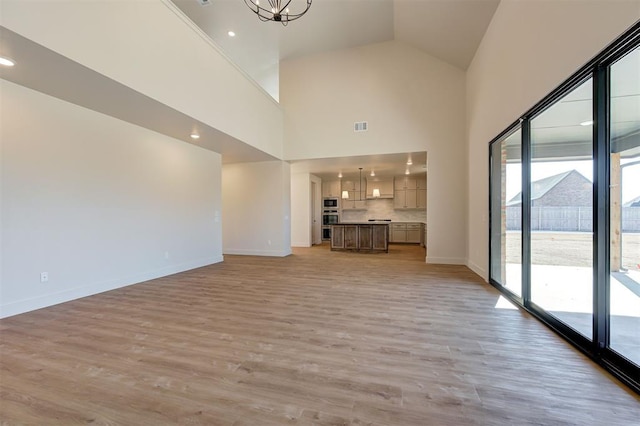 unfurnished living room with high vaulted ceiling, a notable chandelier, and light hardwood / wood-style floors