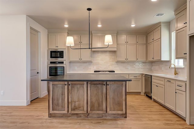 kitchen with decorative light fixtures, a center island, sink, stainless steel oven, and light wood-type flooring