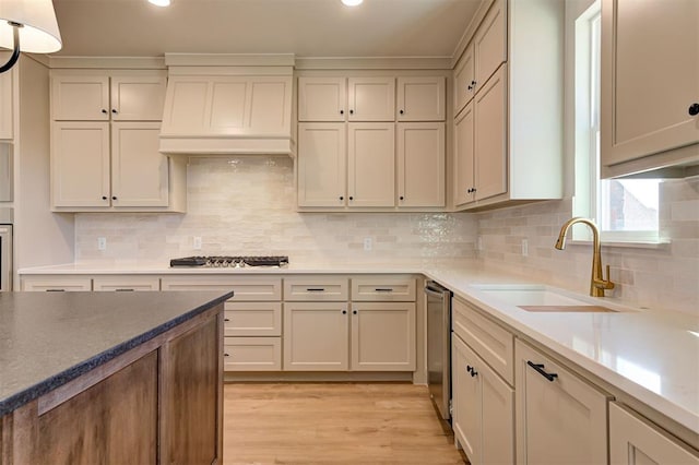 kitchen featuring backsplash, sink, light wood-type flooring, appliances with stainless steel finishes, and custom range hood