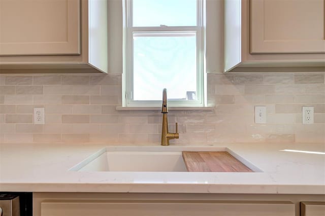 kitchen with light stone countertops, decorative backsplash, and sink