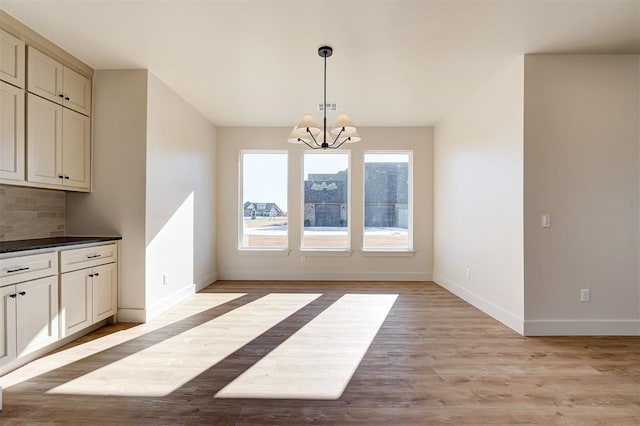 unfurnished dining area with a notable chandelier and light hardwood / wood-style flooring