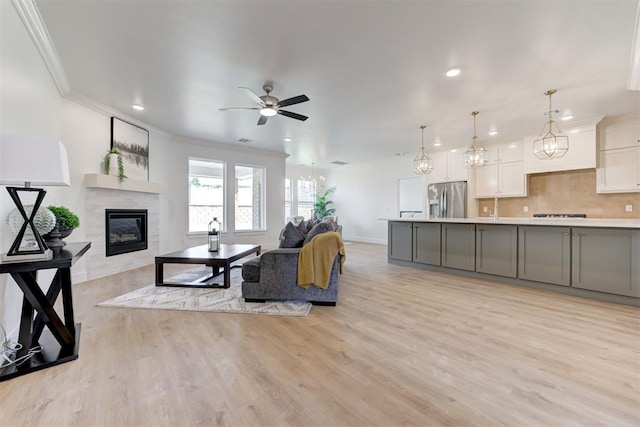 living room featuring a tile fireplace, ceiling fan with notable chandelier, ornamental molding, and light hardwood / wood-style floors