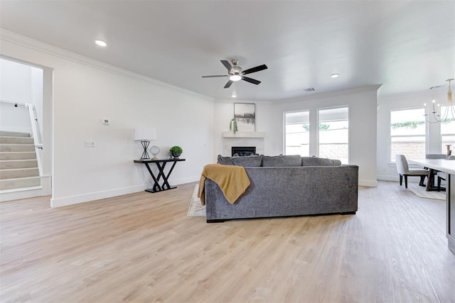 living room with light wood-type flooring, ornamental molding, and ceiling fan with notable chandelier