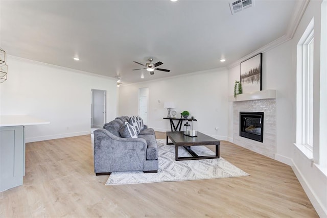 living room with light wood-type flooring, ceiling fan, crown molding, and a tile fireplace