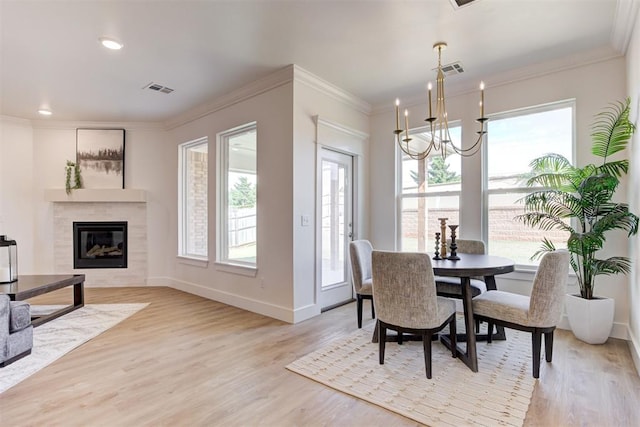 dining area with a tiled fireplace, an inviting chandelier, crown molding, and light hardwood / wood-style floors