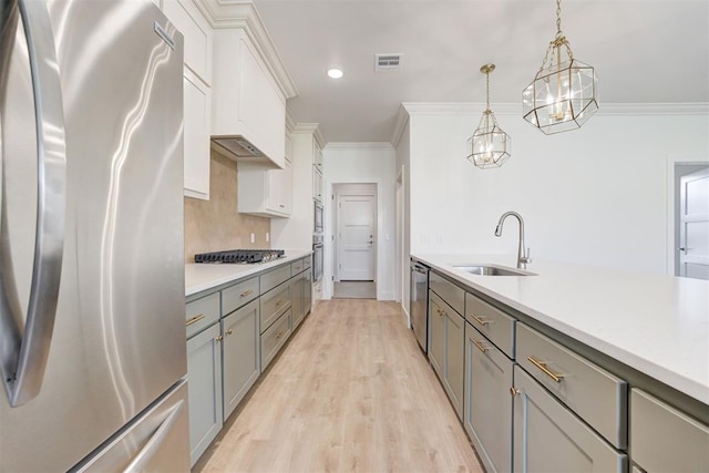 kitchen featuring white cabinetry, stainless steel appliances, hanging light fixtures, crown molding, and sink