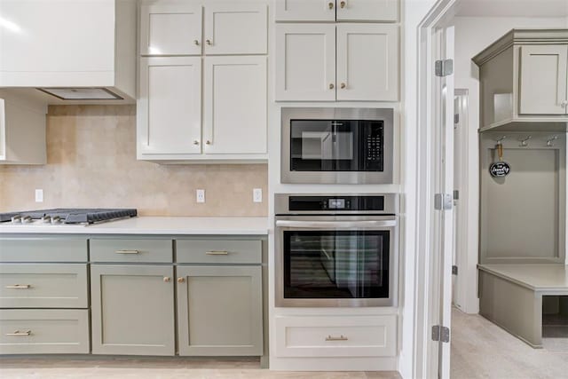 kitchen with backsplash, appliances with stainless steel finishes, premium range hood, and gray cabinets