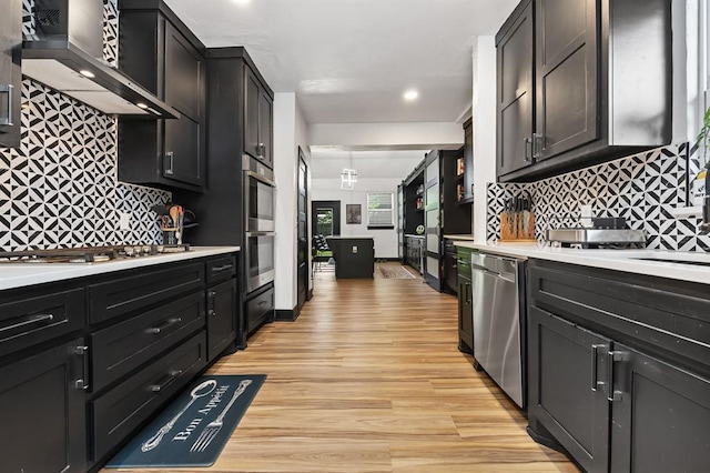 kitchen with tasteful backsplash, appliances with stainless steel finishes, wall chimney exhaust hood, and light hardwood / wood-style floors