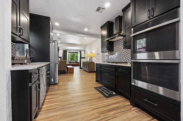 kitchen featuring sink, light wood-type flooring, appliances with stainless steel finishes, decorative backsplash, and wall chimney range hood