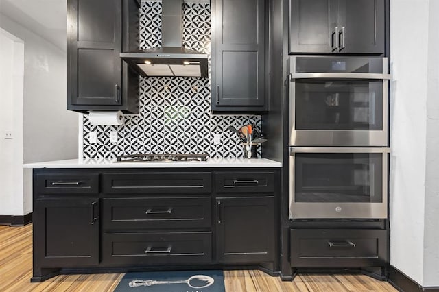 kitchen featuring wall chimney exhaust hood, stainless steel appliances, light wood-type flooring, and backsplash