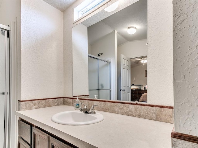 bathroom featuring vaulted ceiling, a textured ceiling, walk in shower, and vanity