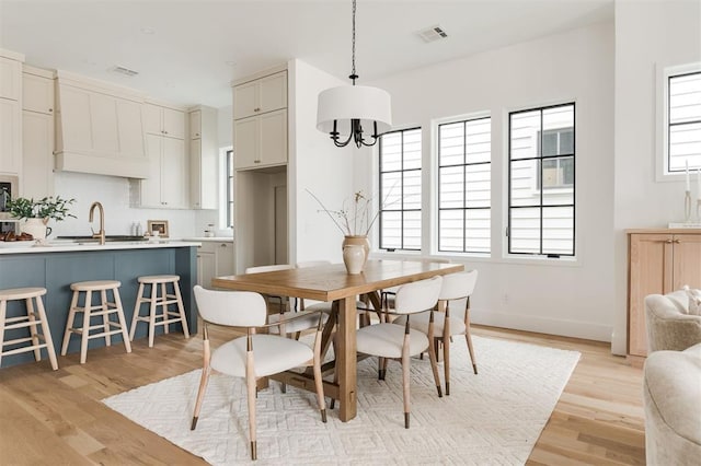 dining area featuring light wood-type flooring, a notable chandelier, and sink