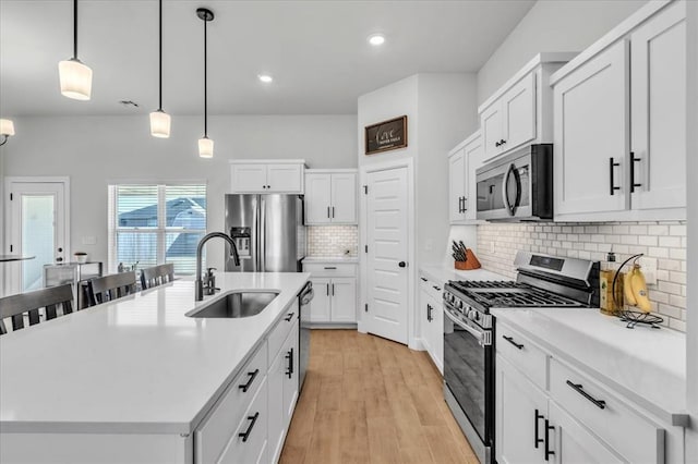 kitchen with appliances with stainless steel finishes, an island with sink, sink, white cabinets, and hanging light fixtures