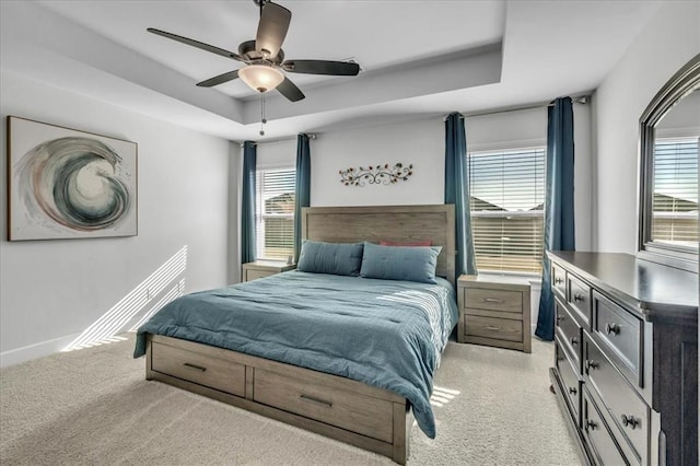 bedroom with ceiling fan, a tray ceiling, light carpet, and multiple windows