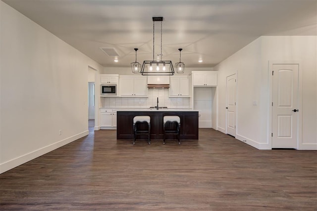 kitchen featuring white cabinetry, a center island with sink, decorative light fixtures, a kitchen breakfast bar, and black microwave