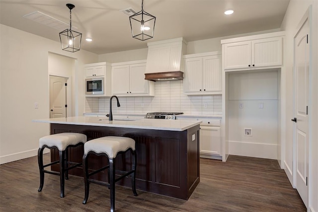 kitchen with pendant lighting, dark wood-type flooring, black microwave, an island with sink, and premium range hood